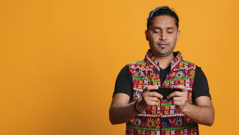 hombre jugando a videojuegos en el teléfono móvil en modo paisaje, fondo de estudio