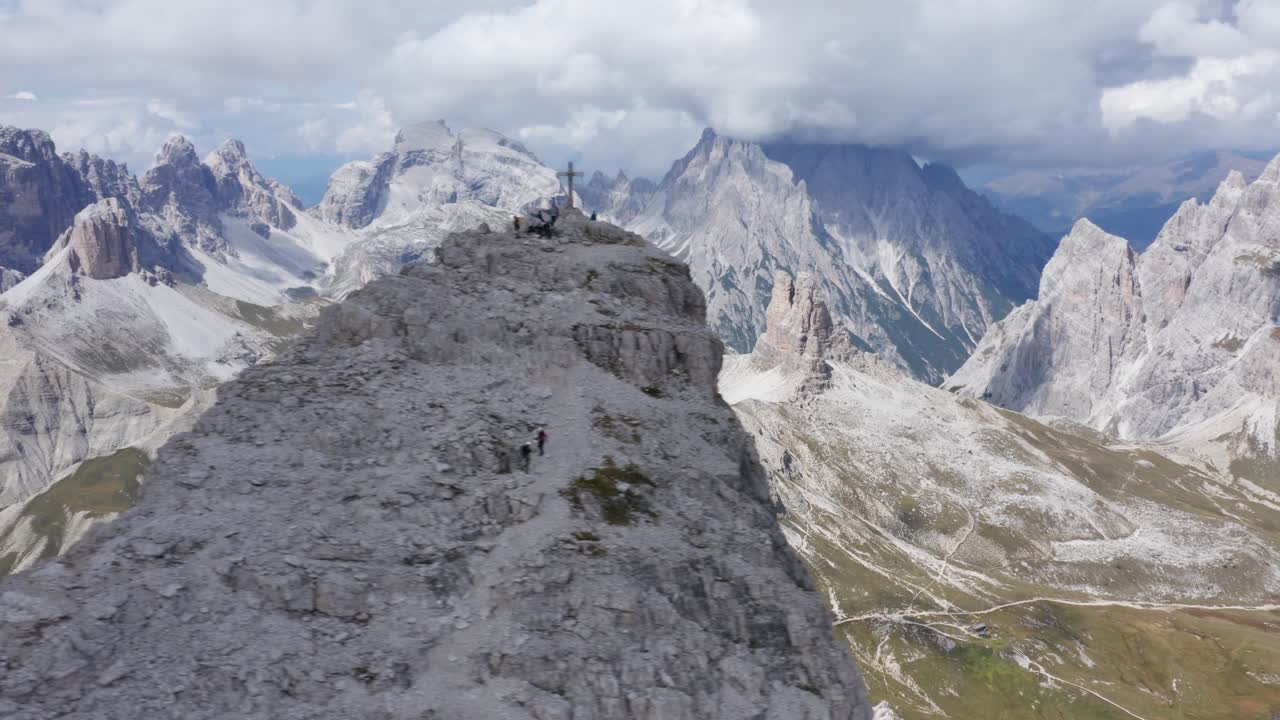 toma aérea que muestra la cruz de la cumbre en el pico de la montaña rocosa - hermoso panorama de la cordillera en el fondo - monte paterno y vía ferrata de luca innerkofler en italia