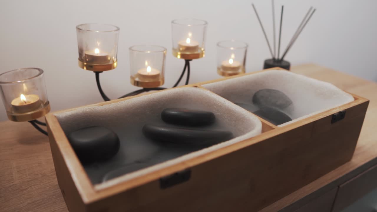 pierres de massage noires dans une boîte en bois, sur fond de belles bougies allumées sur une commode