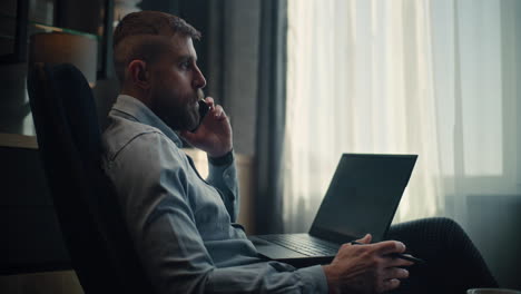 serious stock exchange trader having phone call with investor, using laptop, monitoring real-time stocks and market charts in online trading app. professional investment agent in office. dolly shot.