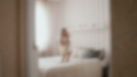 Blurry-shot-of-a-happy-young-girl-with-a-doll-jumping-and-falling-on-a-white-bed