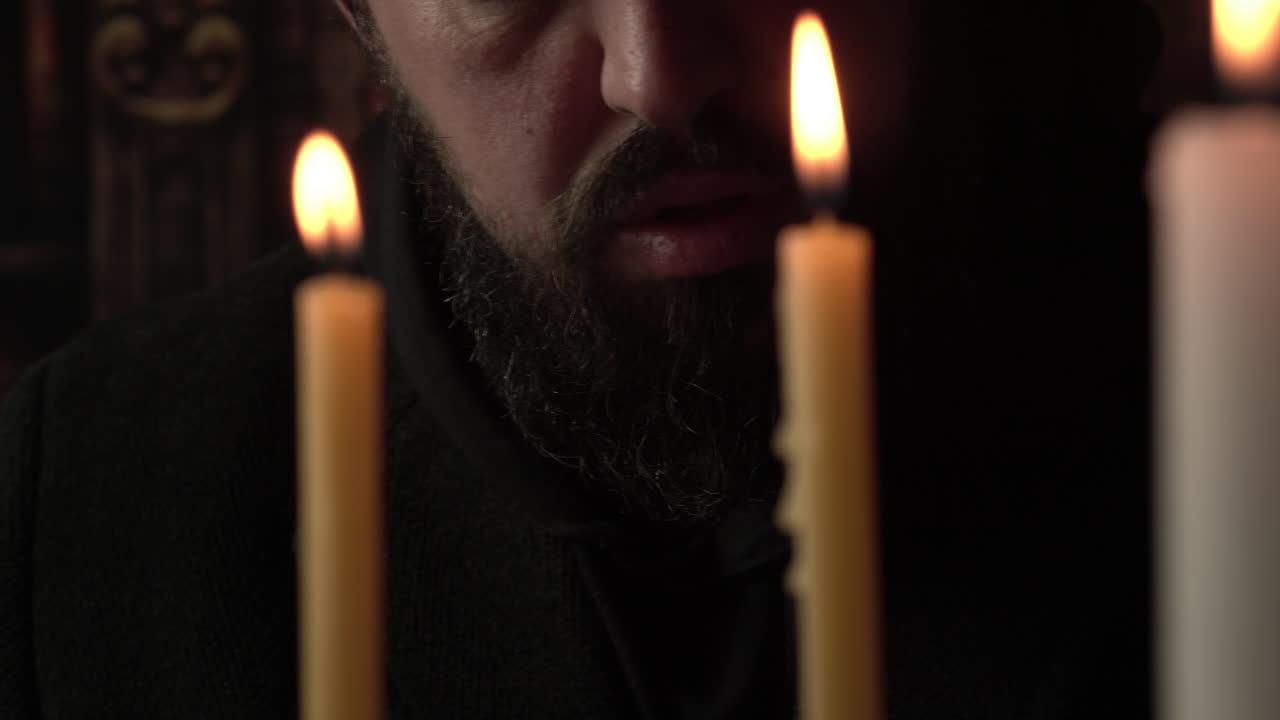 Uomo con la barba che legge un libro davanti a candele, primo piano