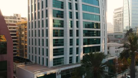 Pedestal-Drone-shot-of-modern-building-between-palms,-Santiago,-Chile