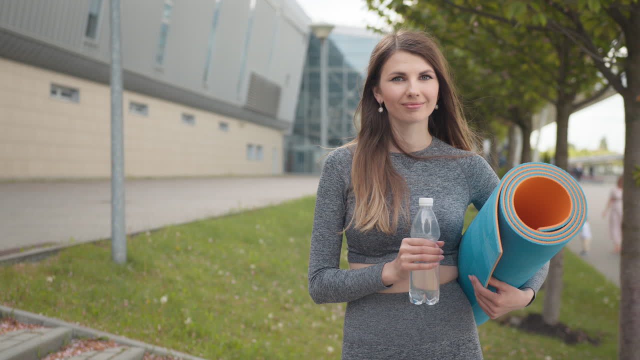 mujer con alfombra de yoga y botella de agua al aire libre