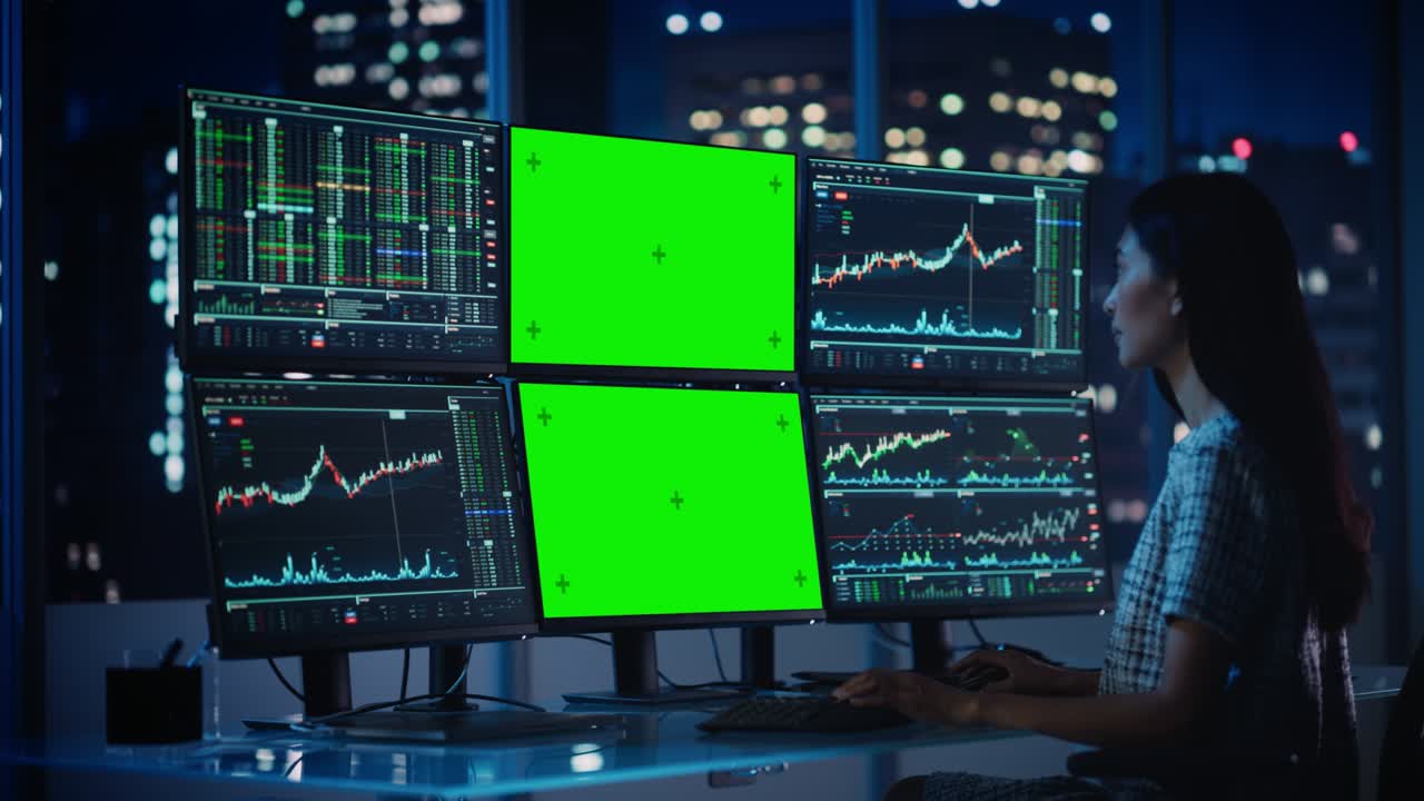 Financial Analyst Working on Computer with Multi-Monitor Workstation with Green Screen Chroma Key Mock Up Template and Real-Time Stock Charts. Businesswoman Works in Investment Bank in the Evening.