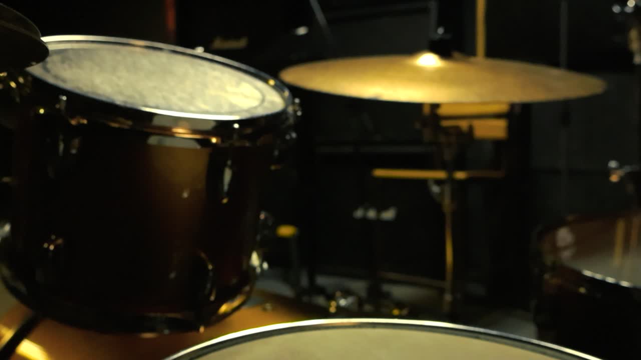 Gorgeous close up footage of an acoustic drum set and golden bronze cymbals behind it and in the foreground with the background studio being blurry indoors at a studio or band rehearsal room, amps.