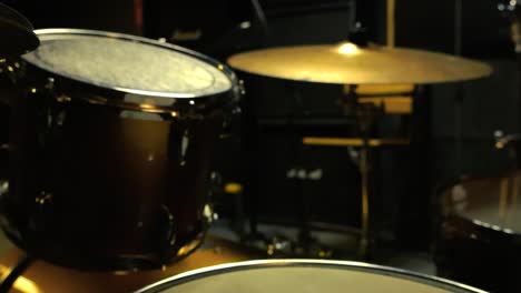 gorgeous close up footage of an acoustic drum set and golden bronze cymbals behind it and in the foreground with the background studio being blurry indoors at a studio or band rehearsal room, amps.