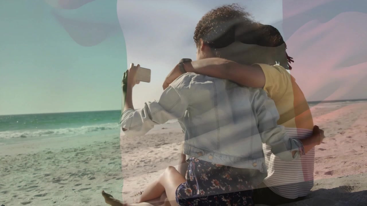 Pareja abrazándose y usando un smartphone en una playa soleada, mostrando marketing con iconos de corazones flotantes