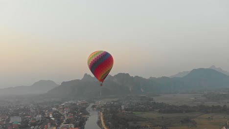 Drone-shot-of-colourful-hot-air-balloon-above-vang-vieng-Laos-with-sunrise,-aerial