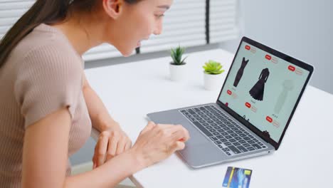 joven asiática usa computadora portátil para comprar productos vender en línea. atractiva chica hermosa con tarjeta de crédito en las manos comprando y comprando bienes en el sitio web en teléfono inteligente. concepto de comercio electrónico.