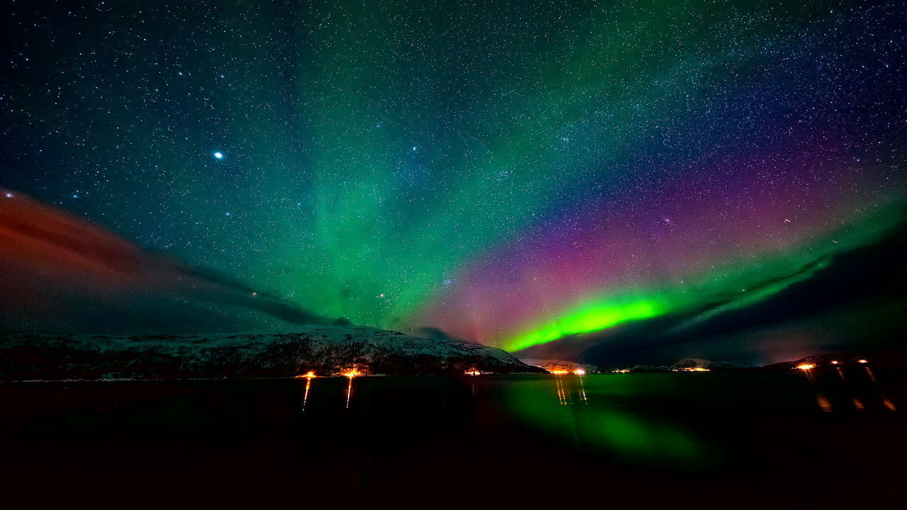 Levende nordlys danser over havet i Mikkelvika, Ringvassøya, nær Tromsø, Nord-Norge. En spektakulær tidsforløpsvideo av nordlyset som reflekteres i arktiske farvann