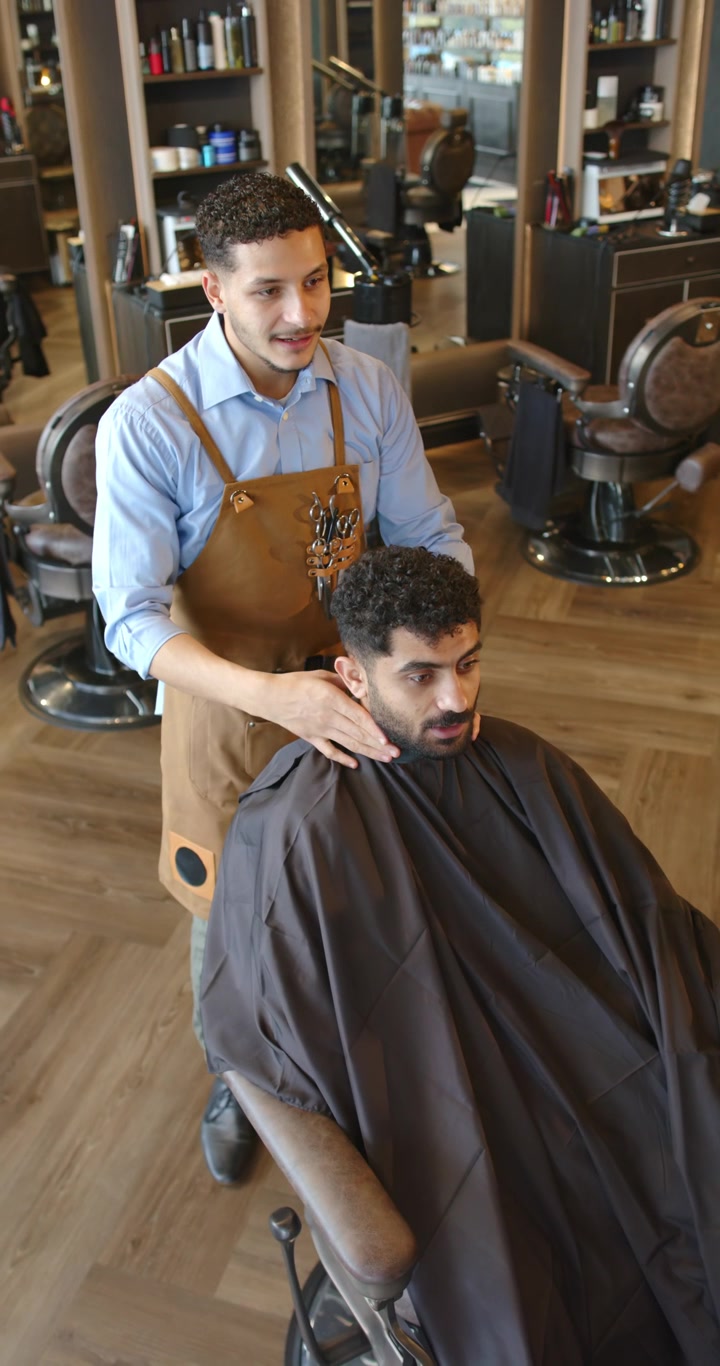 Vertikal video: Afroamerikanske mænd, frisør tjekker nakke og justerer kappe i barbersalon til klipning.
