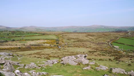 Toma-Panorámica-Lenta-Desde-La-Parte-Superior-De-Un-Tor-Afilado-Que-Muestra-Los-Picos-De-Granito-Y-El-Paisaje-Accidentado-Del-Parque-Nacional-De-Dartmoor-En-Un-Día-Muy-Caluroso