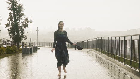 barefoot lady runs and turns with shoes along street at rain