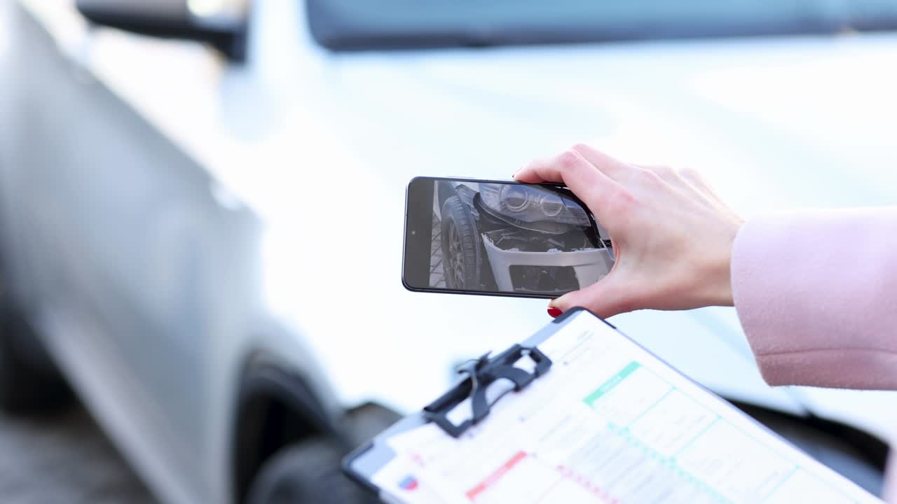 agente de seguros con un documento en las manos y filmando un coche destrozado en la cámara del teléfono película 4k
