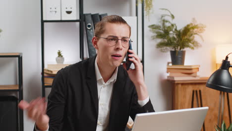 angry young businessman in suit making smartphone online conversation call at home office desk