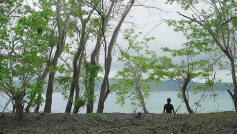 a lone young native spear fisherman walking through trees towards the ocean with his spear gun and equipment to look for fish for dinner