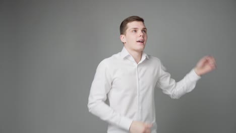 un chico alegre bailando con una camisa blanca sobre un fondo gris.