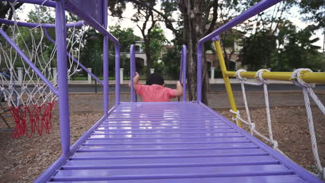 dolly in and out clip of an east asian boy kid having fun playing with colorful playground equipment outdoors