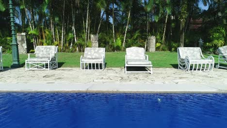 aerial backwards revealing blue water pool and sun loungers in peaceful home