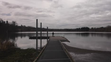 revealing a man using a dlsr camera mounted on a gimbal to record film scenery of a lake at a park with trees sky clouds reflecting off of the surface of the lake water