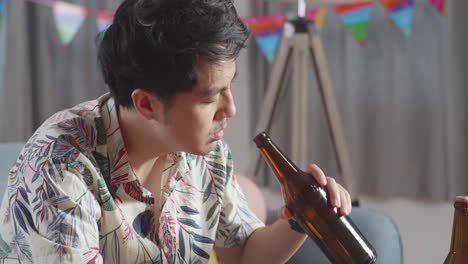 close up of a drunk asian man sitting on a sofa and drinking alcohol while having a party alone at home