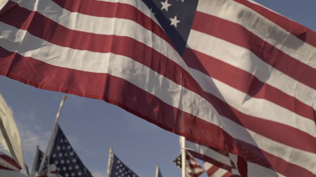 Un primo piano artistico di una bandiera americana che sventola al vento. La texture dettagliata del tessuto rosso, bianco e blu crea una commovente e patriottica dimostrazione di orgoglio e onore nazionale