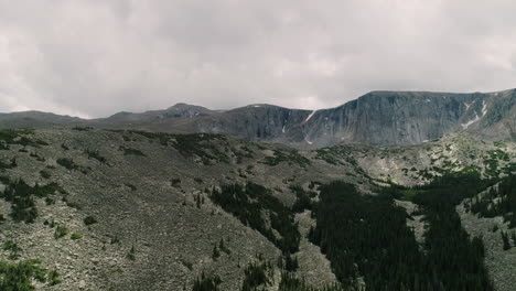 Aerial-of-lake-in-basin-of-pine-covered-mountains-and-in-the-distance-snow-covered-peaks