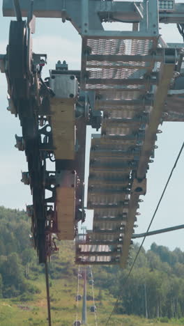 high aerial poma lift support with crossarms against mountain slope with pine forest clearing under blue sky on sunny day bottom view from gondola slow motion