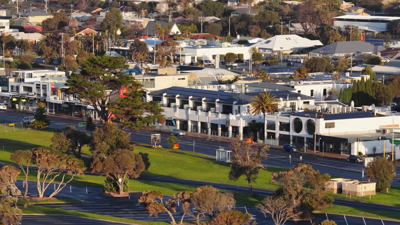 Drone pans above Rye, Melbourne, showing commercial buildings, trees, and streets in golden sunlight