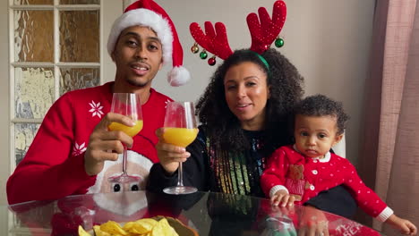 young parents with small child on christmas video call celebrating and raising glasses to camera