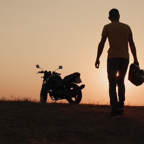 A-man-with-a-helmet-in-his-hand-walks-to-his-motorcycle-at-sunset-1