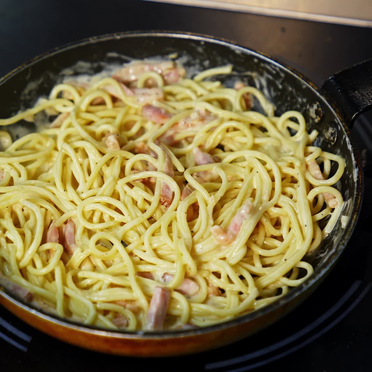 Frying pasta with bacon in tasty sauce. Cooking tasty dish in a frying pan. Chef cooks spaghetti pasta in a restaurant kitchen. Food ingredient. Cooking on cuisine. Cooked for gourmet