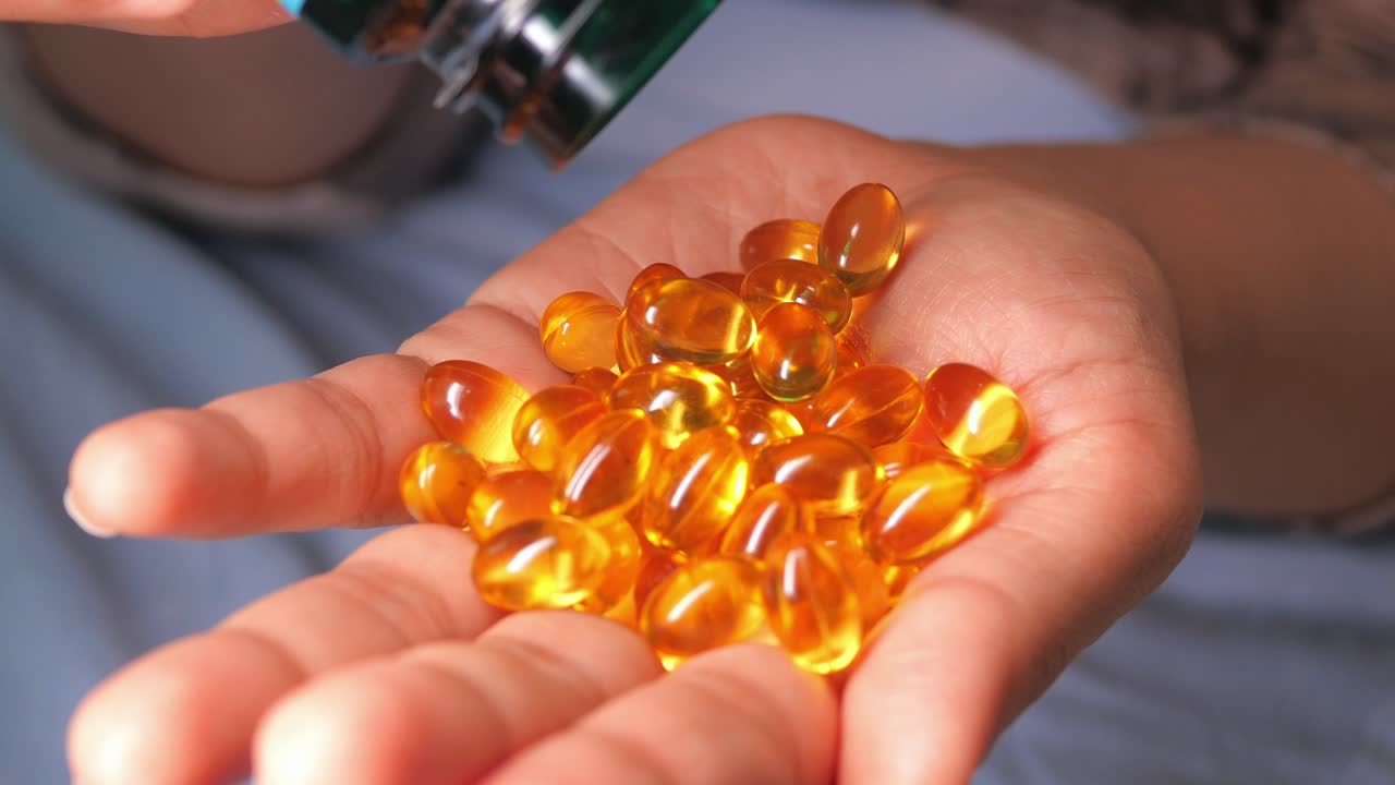 Close-up of Hand Pouring Yellow Vitamin Capsules from Bottle