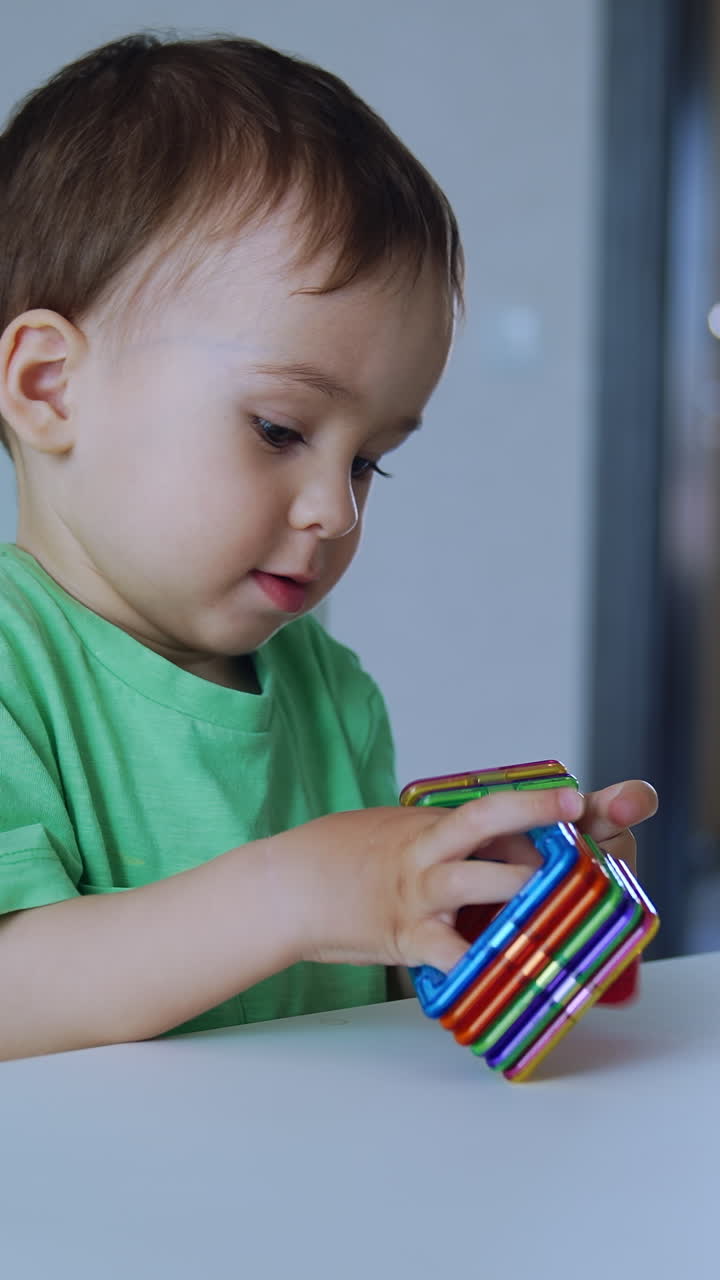 Lovely child playing with bright toys at the table. Baby boy bangs the toys by the table and shoves them by the surface. Vertical video