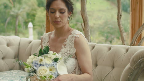 medium shot of a bride sitting on an elegant sofa, raising her hand to look at her engagement ring. a subtle gesture full of emotion and tenderness.