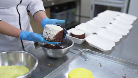miniature cake decoration. confectionary worker covers little cake with chocolate crumbs. food factory for desserts production.