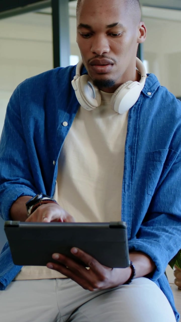 Vertikal video: Holder tablet, siddende mand i blå skjorte taster, læser på kontoret iført headset
