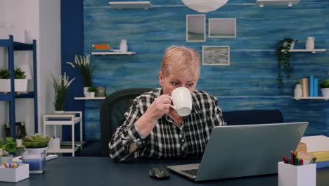 senior woman enjoying a cup of coffee while working on laptop