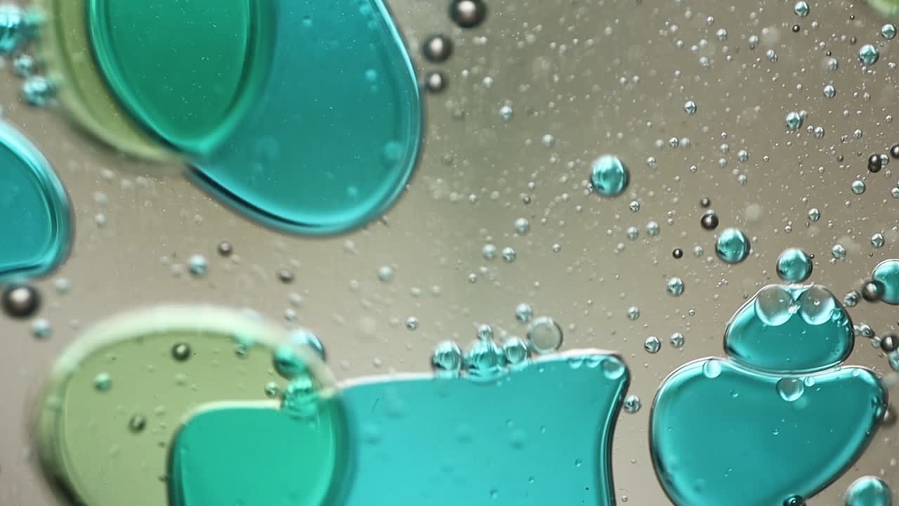 Close-up of blue and green liquid with floating bubbles and blobs in motion inside a lava lamp, viewed in a horizontal orientation. Hypnotic and abstract visual texture