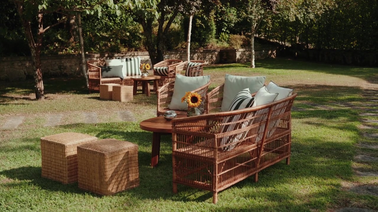 Wicker sofas ottomans and low tables arranged on grass under trees at an outdoor event