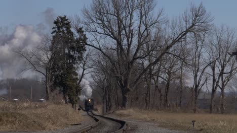 a head on view of a restored antique steam passenger train blowing smoke and steam on a sunny winter day