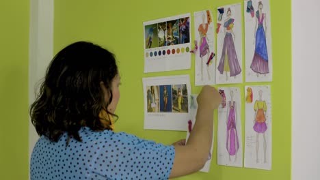 latin fashion designer working and arranging several sketches on the wall for her new collection