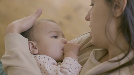 close up shot of an adorable baby girl sucking her thumb and falling asleep while her mother holding her, singing a lullabay and stroking her hair gently 1