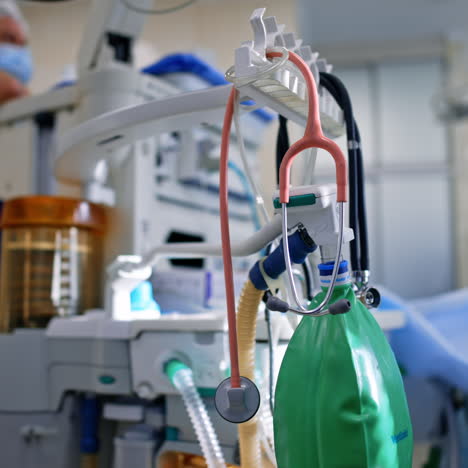doctor's tools hanging on the apparatus. stethoscope and ambu bag are on the modern lung ventilating machine. surgeon works at backdrop in blur.
