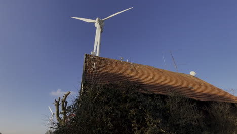 Low-angle-shot-of-old-farm-house-and-rotating-wind-turbine-during-beautiful-weather-with-blue-sky