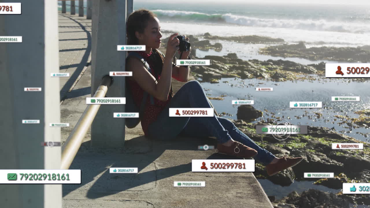 Woman using camera photographing shoreline on pier edge, showing floating social media data icons