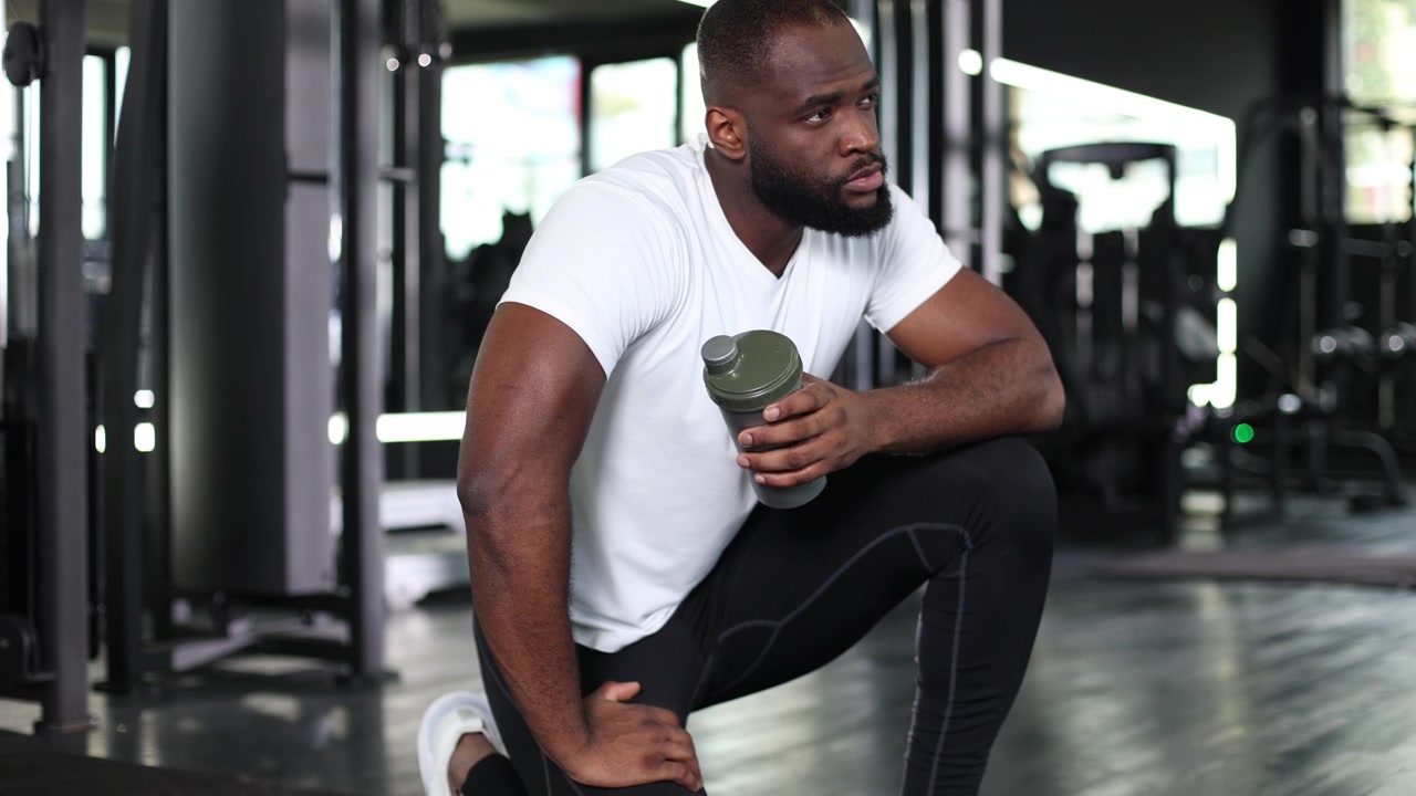 Pria Kulit Hitam Berotot Beristirahat dengan Botol Shaker di Gym