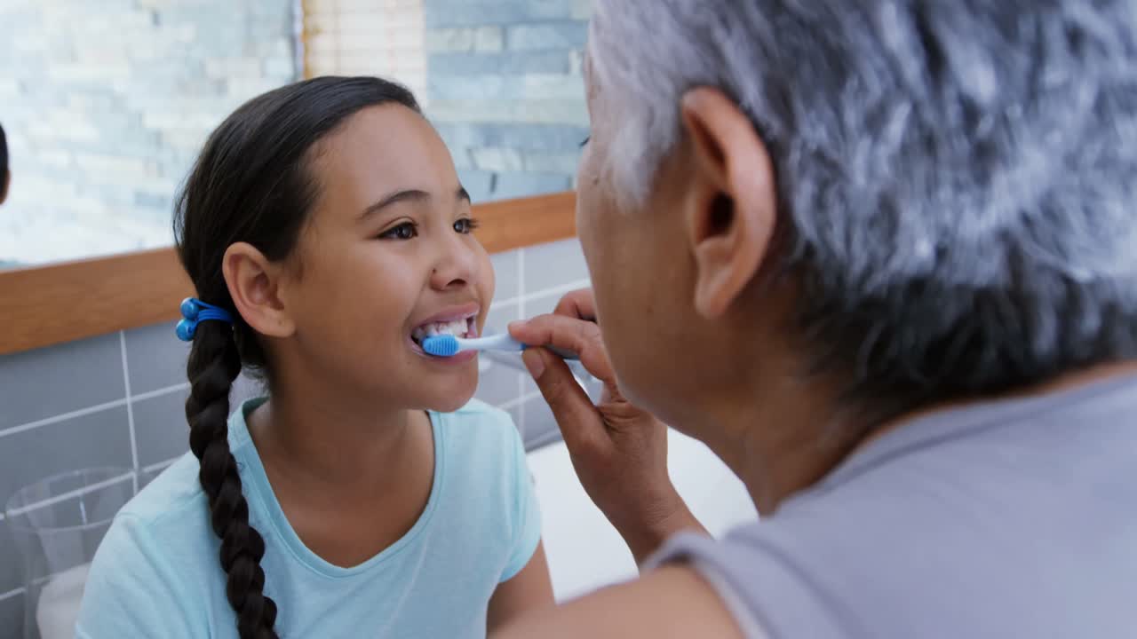 Grandmother helping granddaughter to brush her teeth in the bathroom 4k