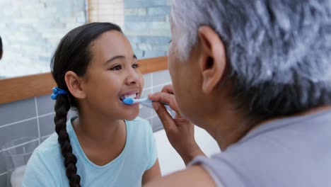 grandmother helping granddaughter to brush her teeth in the bathroom 4k